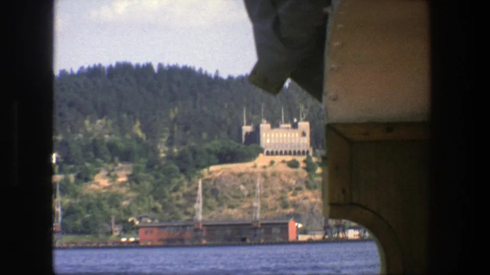 1975 Stockholm waterfront view with the pale hillside building and red rail car partially framed by the boat structure.