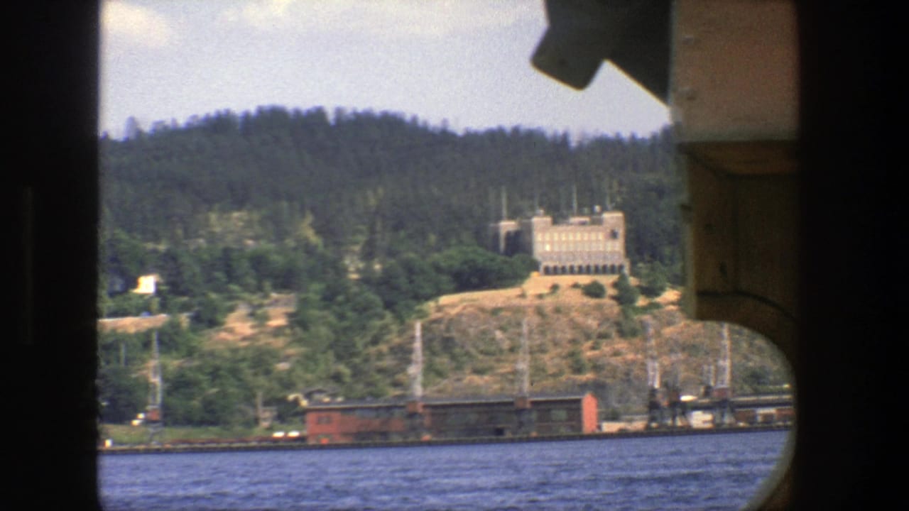 Waterfront hillside with a tan building, rail cars, and boat framing at the edges.