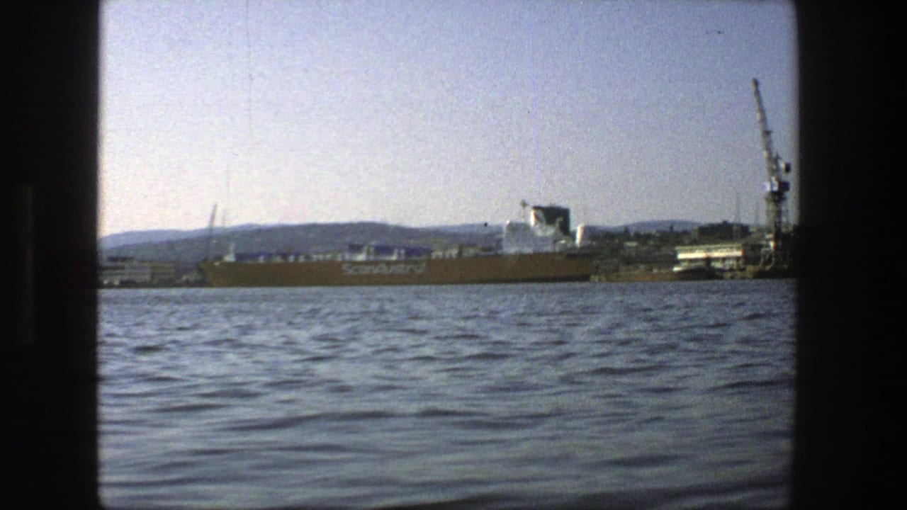 Cargo ship passing a Stockholm harbor dock with crane and rippled water in foreground.
