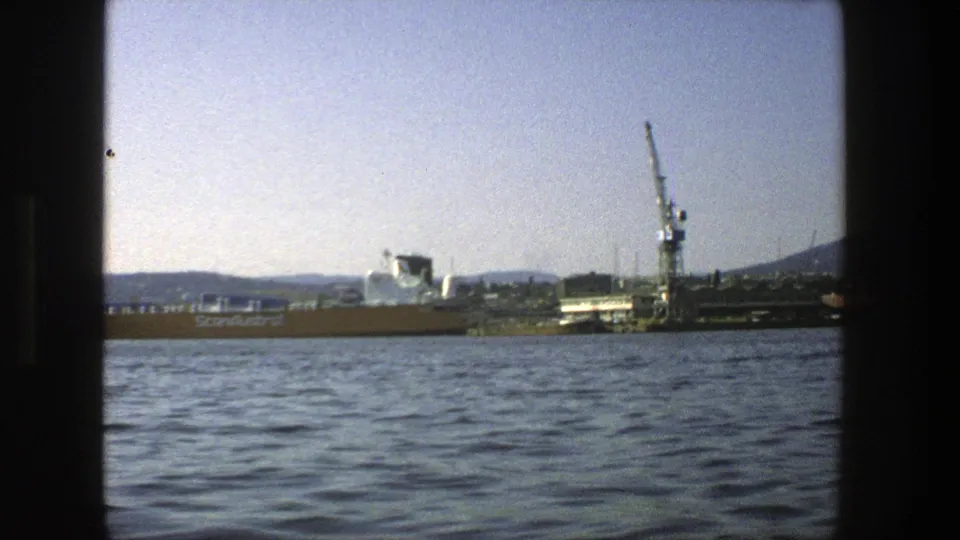 1975 8mm Stockholm harbor frame showing the ScanAustral vessel near a crane, with rippled water and hills in the distance.