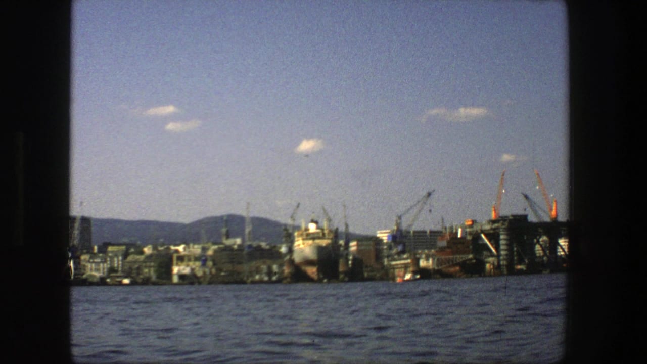1975 Stockholm harbor view from the water, with a large vessel, industrial cranes, waterfront buildings, distant hills, and dark frame edges.