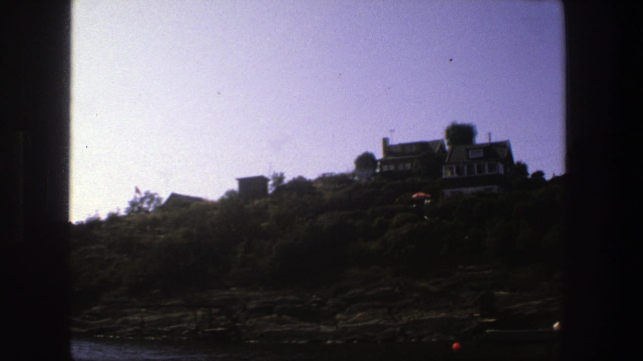 Hillside houses and trees above rocks, with dark borders around the frame.