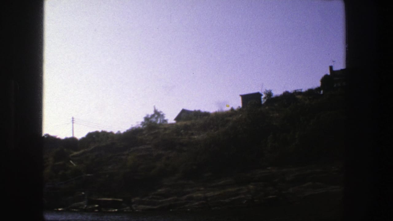 Rocky tree-covered hillside with small houses above water and dark film borders.