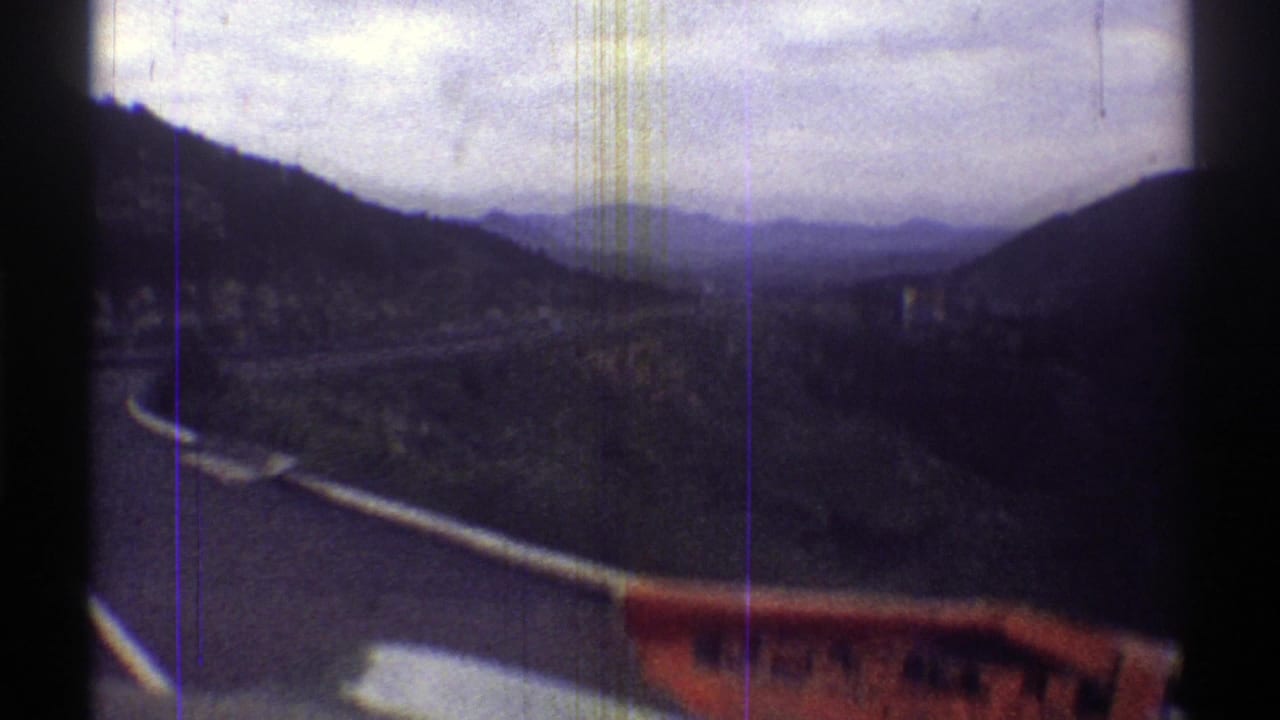 Curving road below dark mountain slopes with a red foreground object at the lower edge.