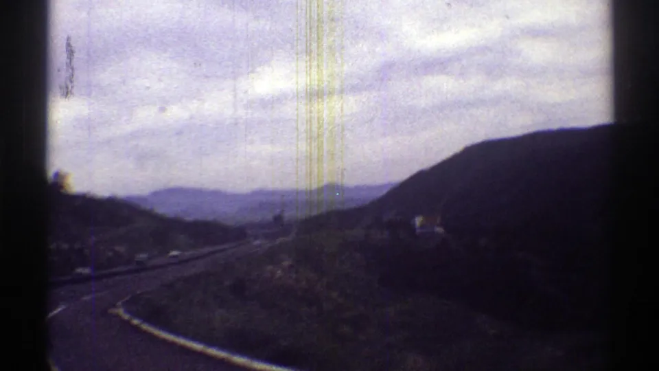 1969 Arizona 8mm view of a winding road along a hillside, with distant ridges, sparse roadside poles, and open valley terrain.
