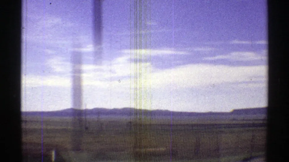 1969 Arizona 8mm frame looking across open desert or valley terrain toward low mountains under a bright, clouded sky.
