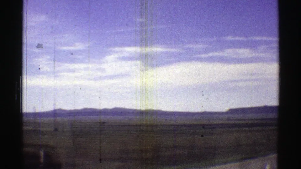 1969 Arizona 8mm view across a broad desert plain, with low mountains on the horizon and film scratches visible in the frame.