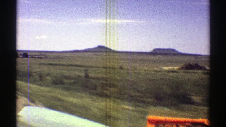 1969 Arizona home-movie view across open desert grassland from a moving car, with low mesas, sky, and windshield film marks.