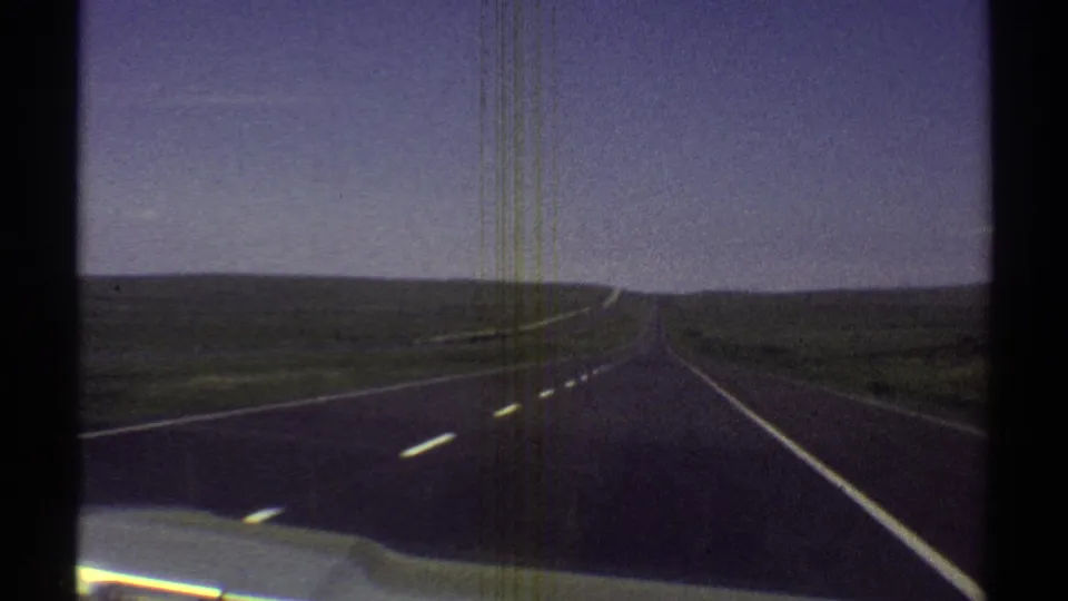 Forward-facing 1969 Arizona 8mm frame showing a paved highway receding through flat desert under a clear sky.