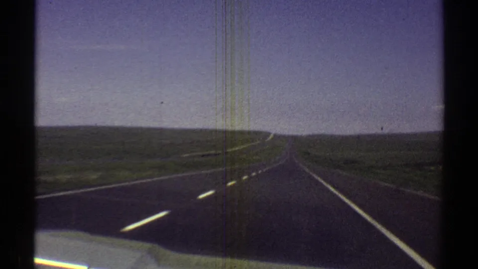 1969 Arizona 8mm frame of an open desert highway with lane markings, low horizon, blue sky, and visible film wear.
