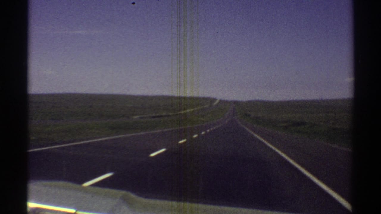 Car-mounted or dashboard view of an Arizona desert highway, with road markings leading toward a distant horizon.