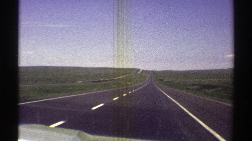 8mm frame of a straight Arizona roadway from inside a moving car, with bright sky and sparse desert on both sides.