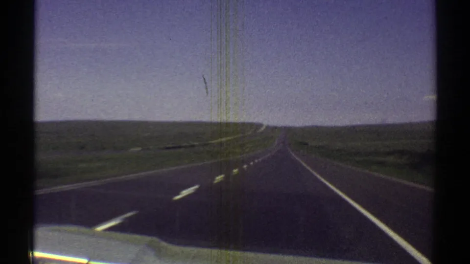 Late-1960s home-movie frame showing an Arizona highway receding toward the horizon from a car interior viewpoint.