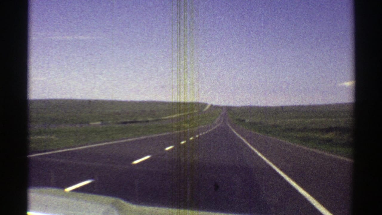1969 Arizona 8mm frame showing a passenger-view drive along a straight rural highway through open fields.