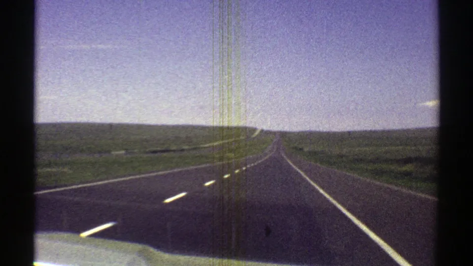 1969 Arizona 8mm frame showing a passenger-view drive along a straight rural highway through open fields.