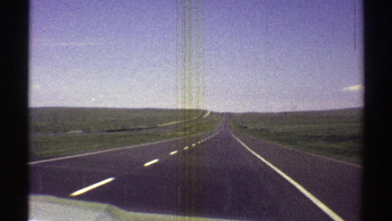 Straight highway receding through open countryside under a bright sky.