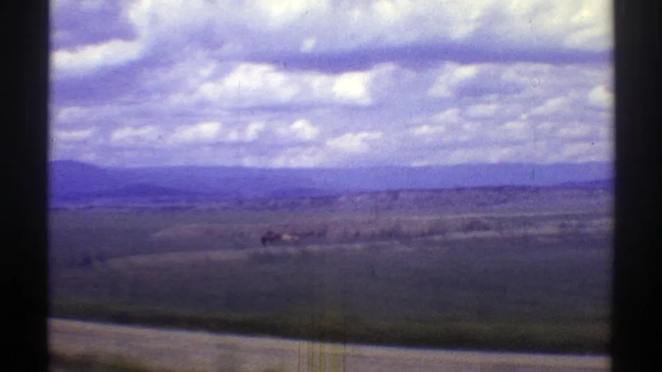1969 Arizona 8mm landscape view with grazing horses, open fields, distant hills, and a cloudy sky.