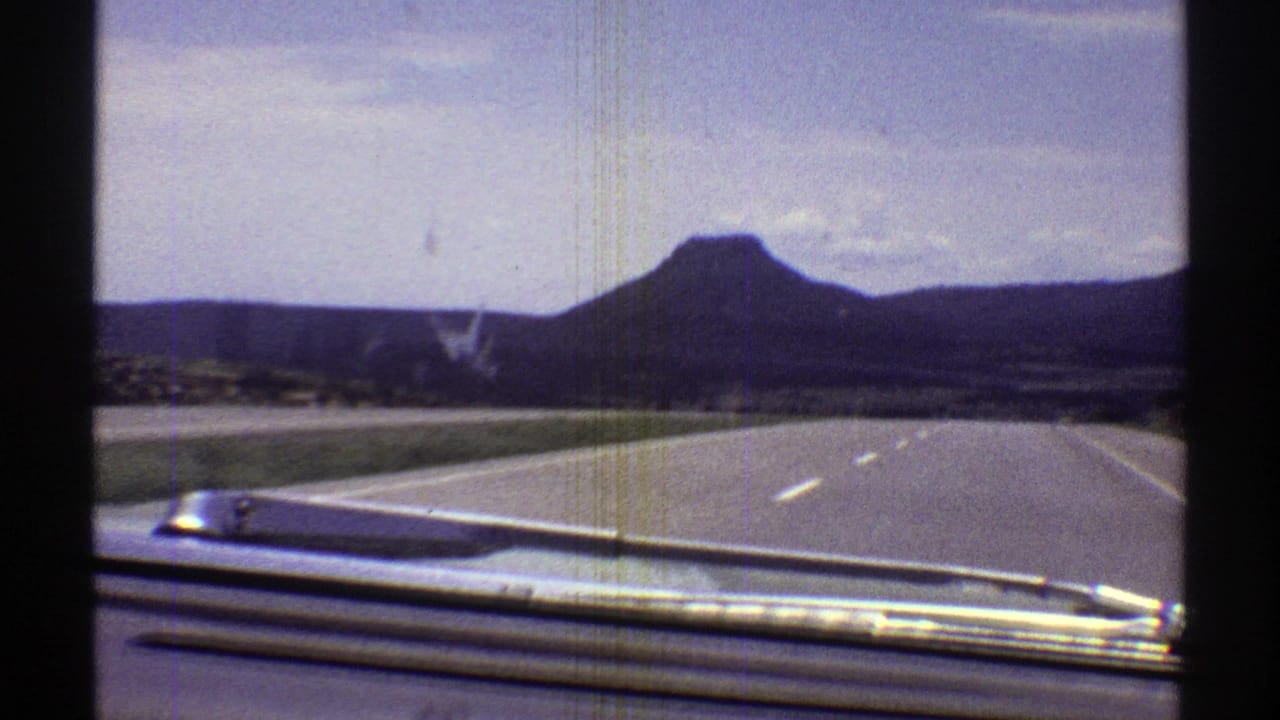 Car hood and highway lanes leading toward a flat-topped mountain under a pale sky.