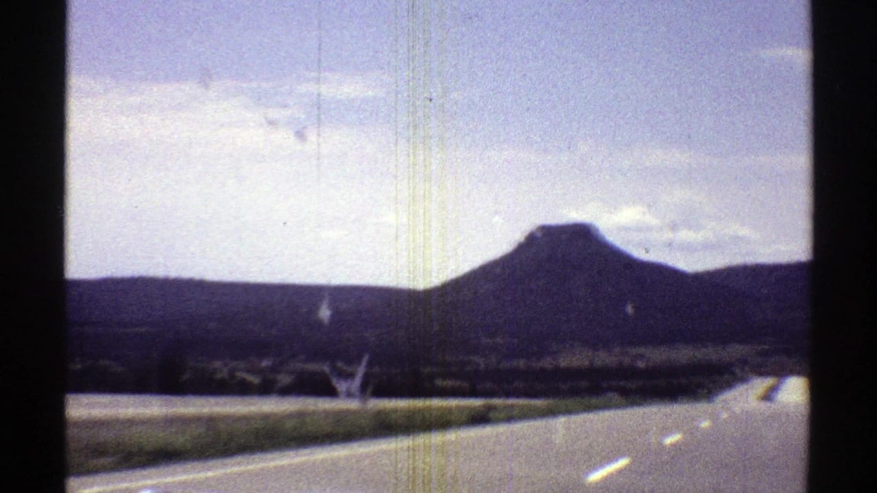 1969 Arizona 8mm frame showing a highway and lane markings viewed from a moving car toward a flat-topped mountain.