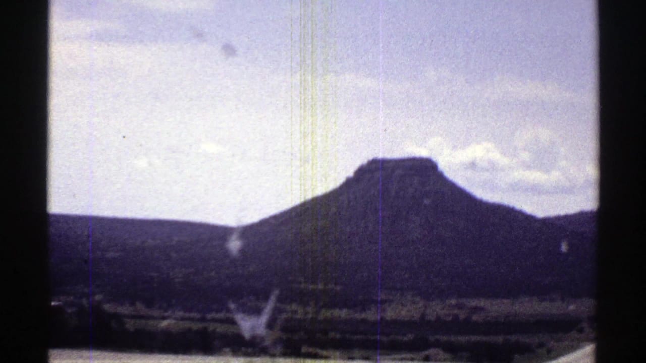 1969 Arizona road-trip view through a car window, showing a flat-topped mountain, low hills, and sparse vegetation.