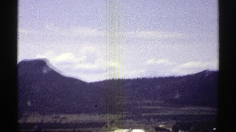 1969 Arizona 8mm travel frame with a low ridge, desert foreground, pale clouds, and dark car-window framing.
