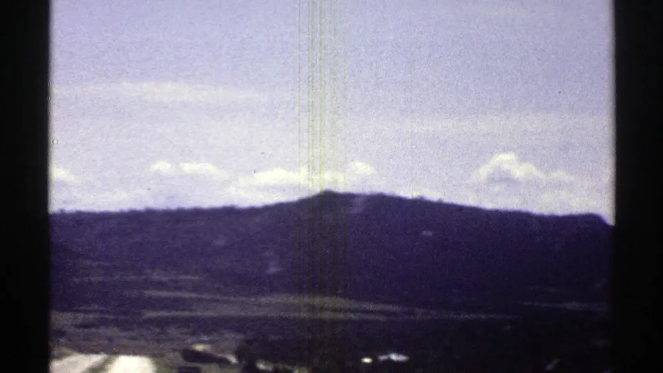 1969 Arizona home-movie frame showing distant hills and open terrain through a vehicle window on faded 8mm film.