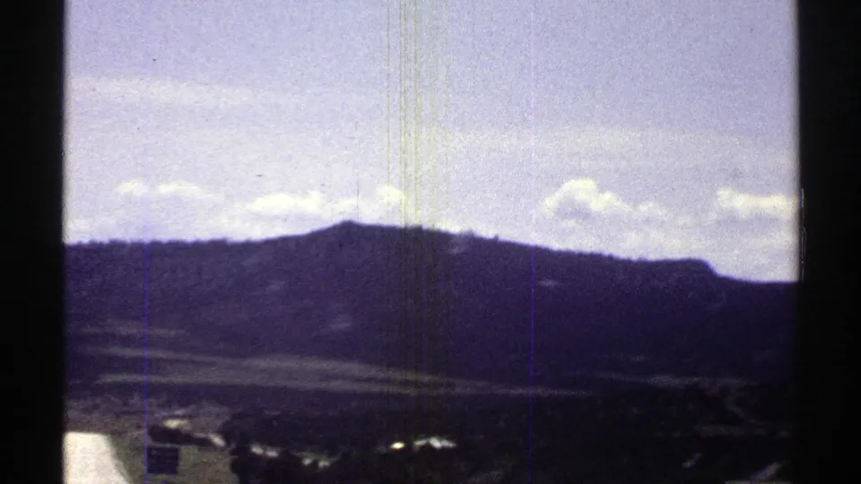 1969 Arizona 8mm frame showing distant mountains and sky from inside a moving car, with dark film borders and scratches.