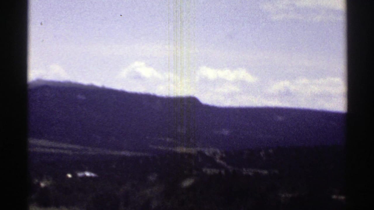Dark mountain slope under a pale sky, framed by vertical film-strip borders.