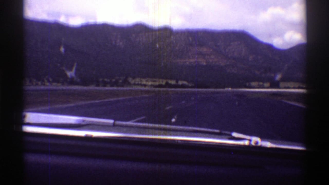 1969 Arizona 8mm road view through a windshield, with a wiper at the bottom and mountains under a cloudy sky.