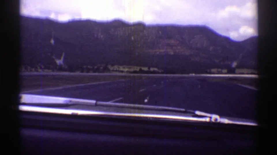 1969 Arizona 8mm road view through a windshield, with a wiper at the bottom and mountains under a cloudy sky.