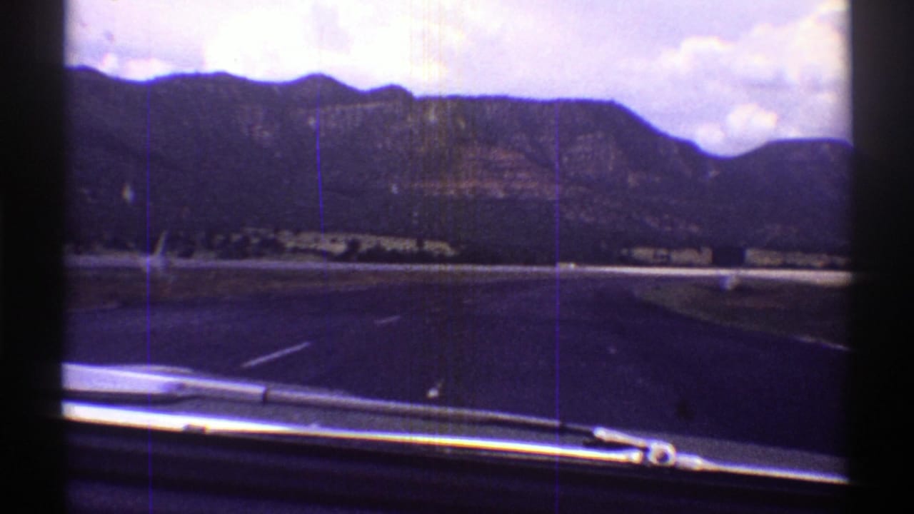 Forward highway view from inside a moving car with mountains ahead.