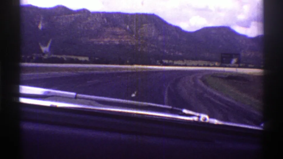 1969 Arizona road-trip frame showing a curving highway, windshield wiper, distant mountains, and cloudy sky.