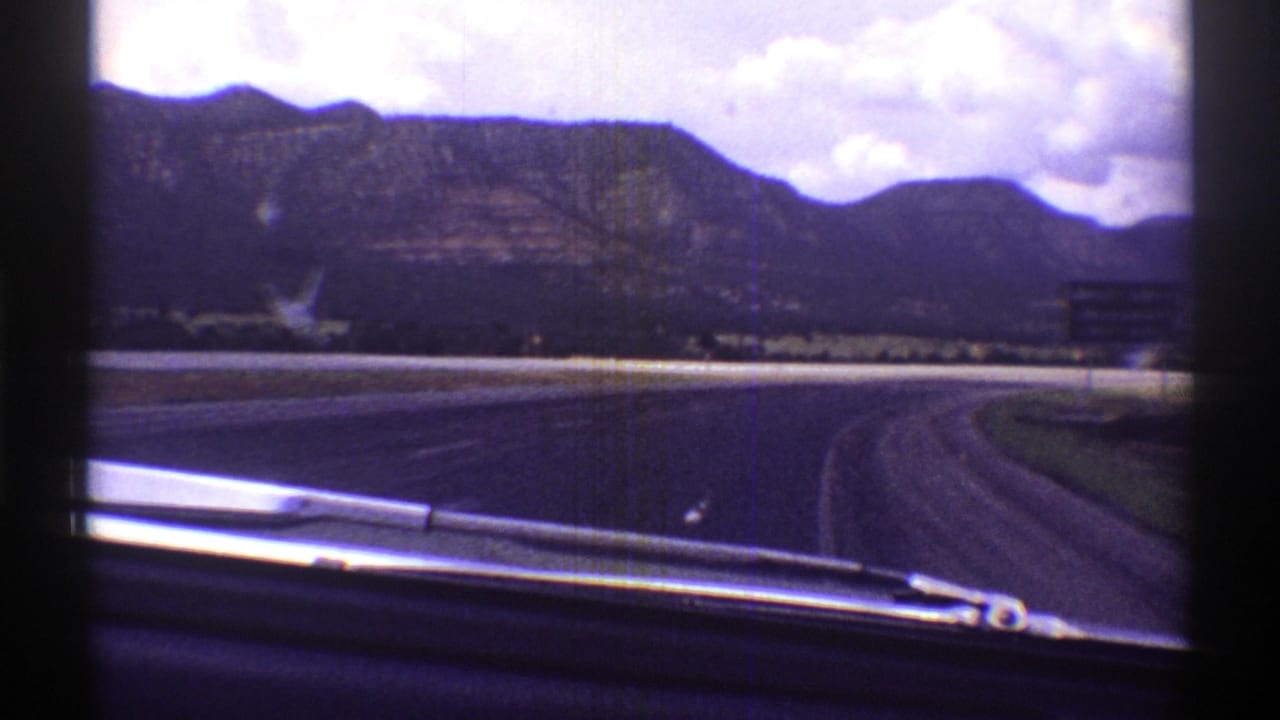 1969 Arizona home-movie view through a car windshield toward a curving highway, mountains, and cloudy sky.