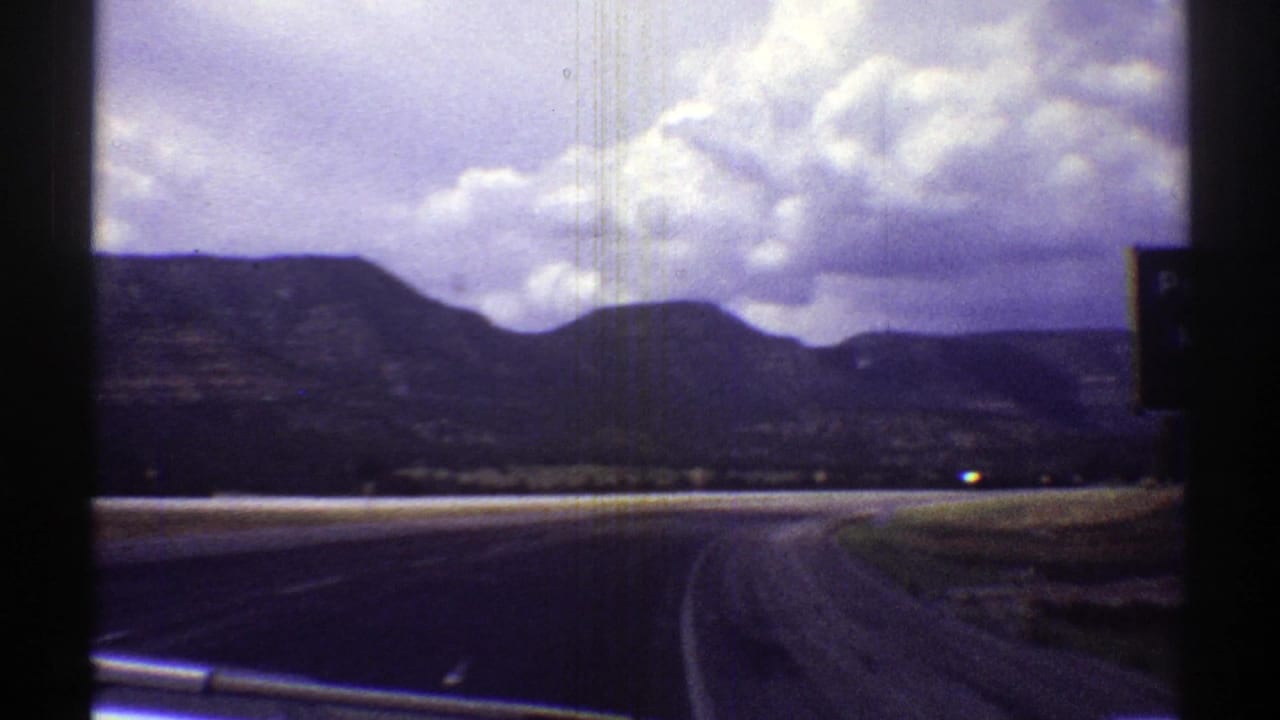 Arizona road landscape viewed from inside a moving car, with mountains, open roadside, and puffy clouds.