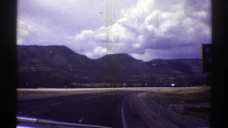 Arizona road landscape viewed from inside a moving car, with mountains, open roadside, and puffy clouds.