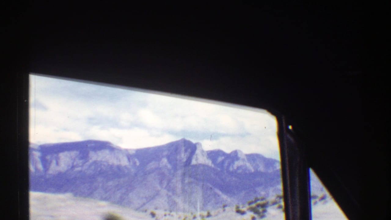 Distant mountains seen through dark car windows from a moving vehicle.
