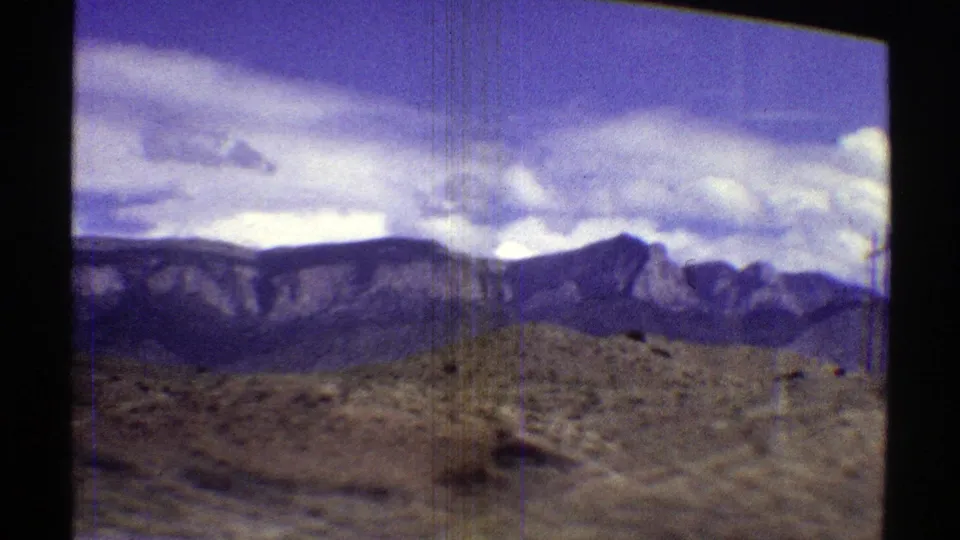 Arizona desert scrub and low roadside terrain pass before rugged mountains in a 1969 home-movie road view.