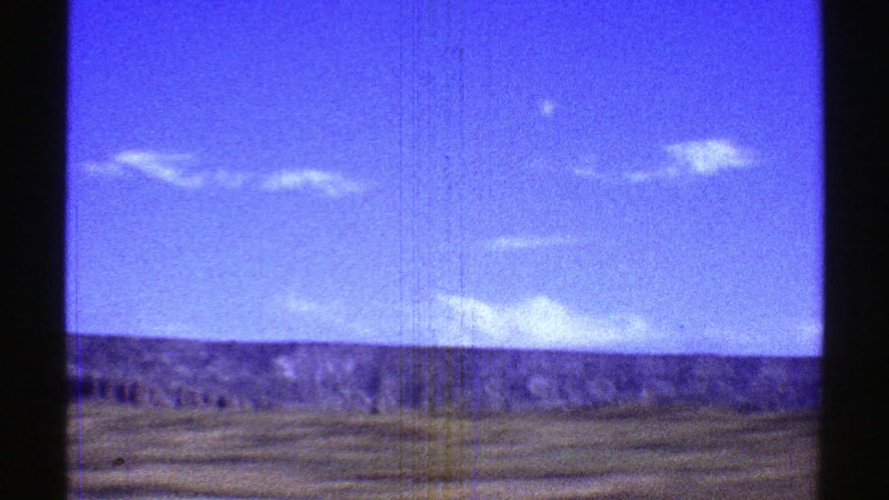 Blue sky and white clouds over a low desert ridge, seen through dark frame edges.