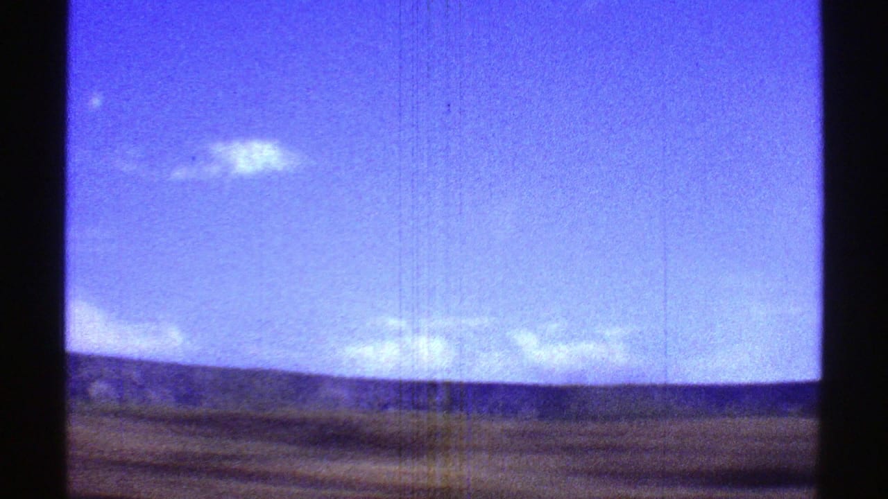 1969 Arizona desert landscape with scattered clouds, a low horizon, and a dark vertical edge from the scanned 8mm frame.