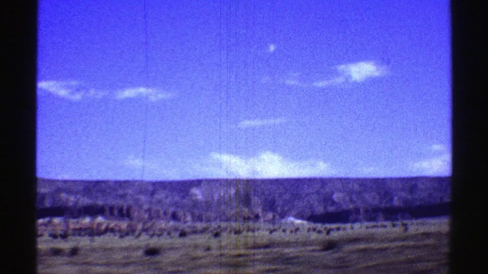1969 Arizona 8mm view of open scrubland, distant hills, blue sky, and clouds, with visible film grain and frame edges.