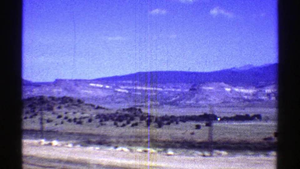 1969 Arizona home-movie frame showing a desert valley, low mountains, open sky, and pale foreground patches in aged 8mm color.