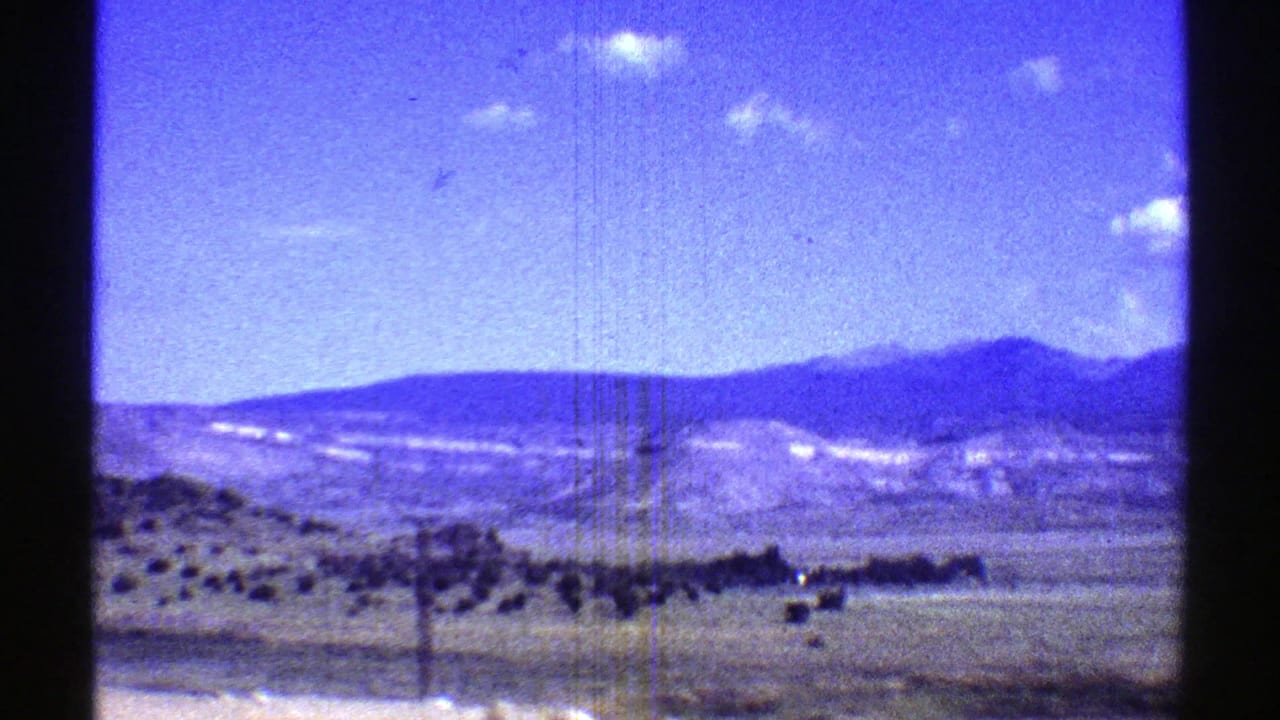 Desert plain and distant mountains under a blue sky seen from a moving vehicle.