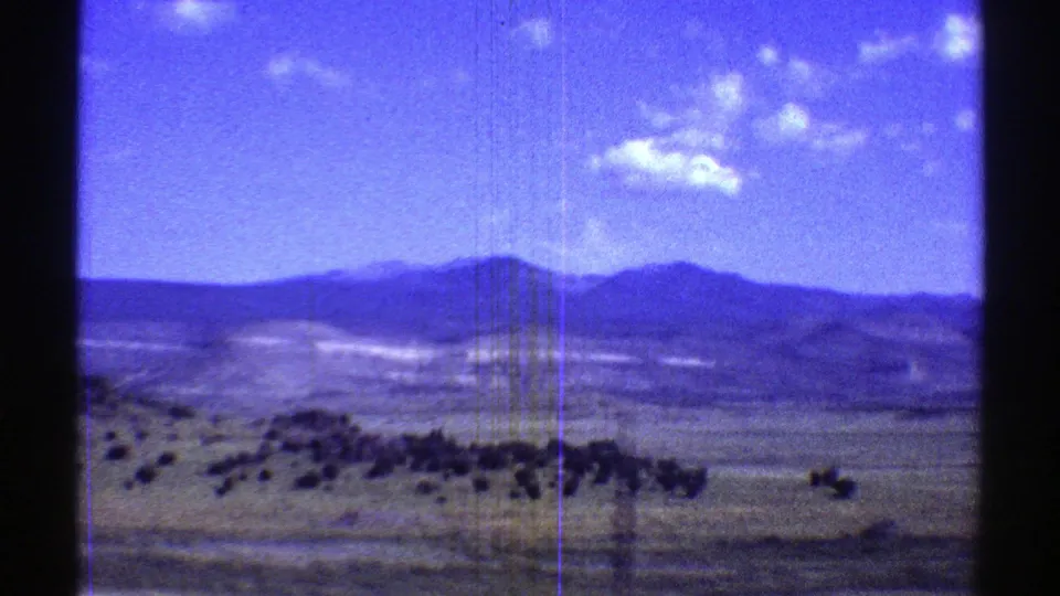 1969 Arizona 8mm frame of rolling arid ground, scrub vegetation, and distant mountains viewed during a moving vehicle pass.