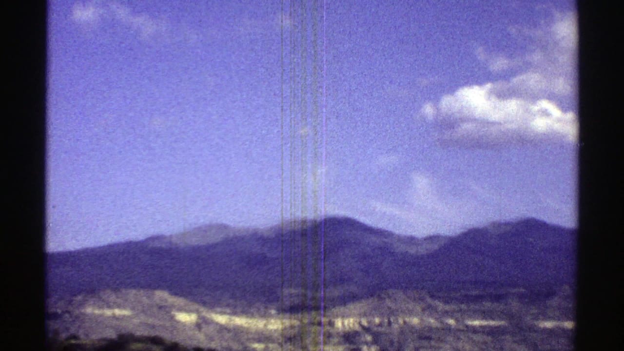 Distant mountain ridge under blue sky with small white clouds and dark film borders.