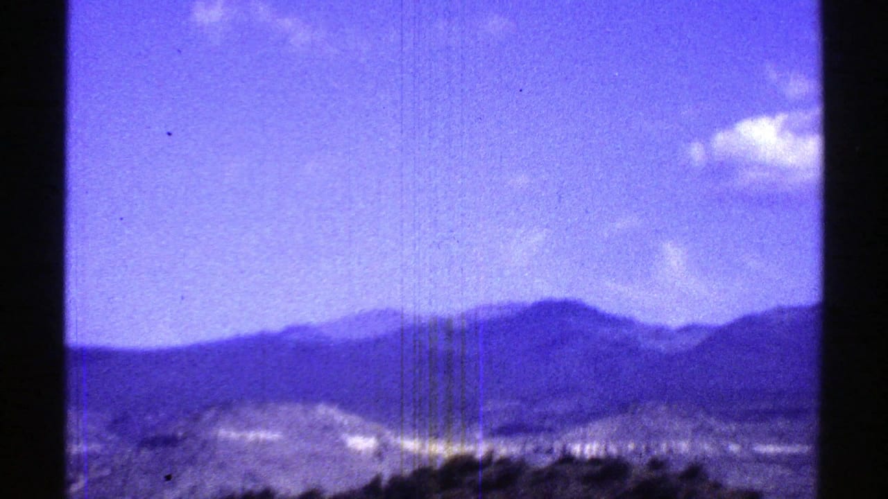 Blue sky and distant mountains above scrubby desert terrain in a soft 8mm frame.