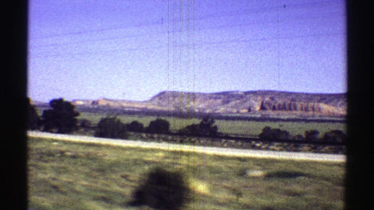 Roadside field with distant low mountains under a blue sky.