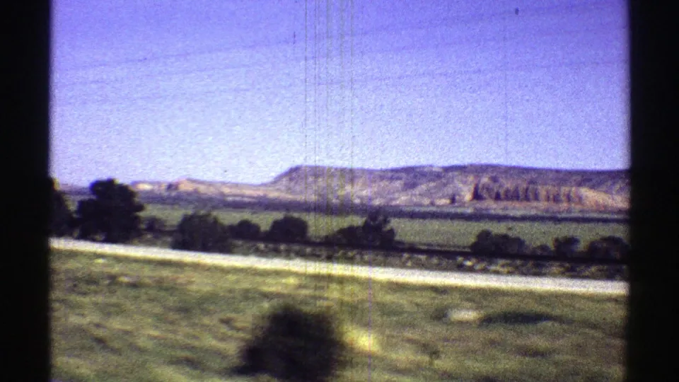1969 Arizona home-movie frame showing a moving roadside view of green fields, trees, and distant layered mesas.