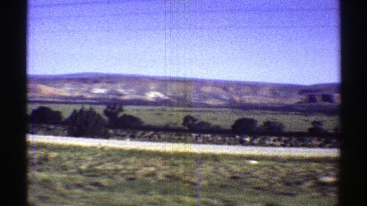 Open field and distant ridge seen through dark film-frame borders.