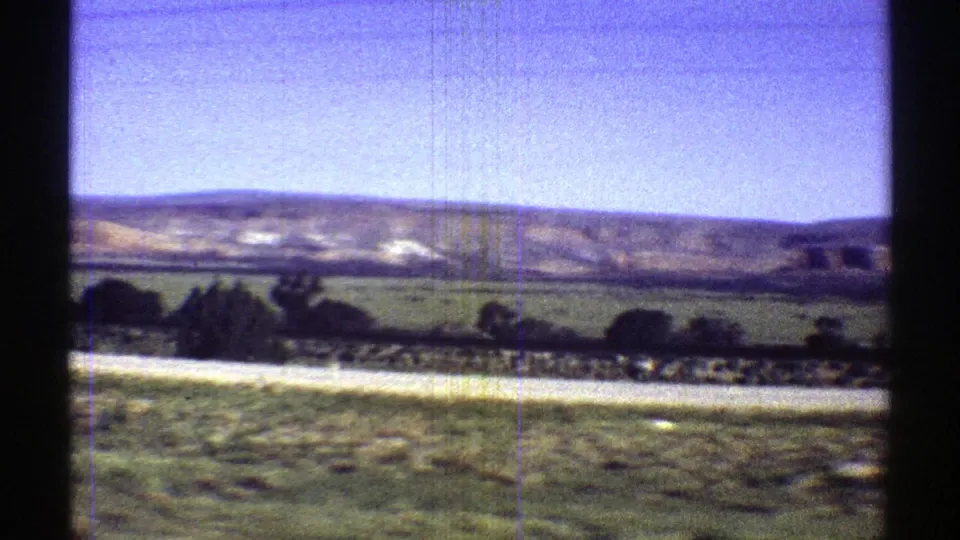 Moving 8mm view of rural Arizona terrain with fields, a distant ridge, blue sky, and visible gate borders.