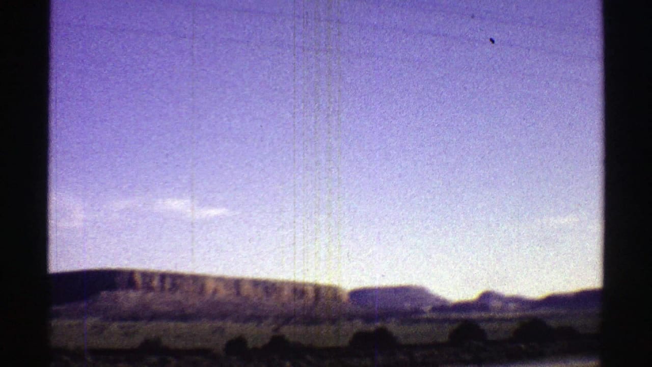 1969 Arizona countryside view with low hills, distant mountains, pale blue sky, and dark interior window framing.